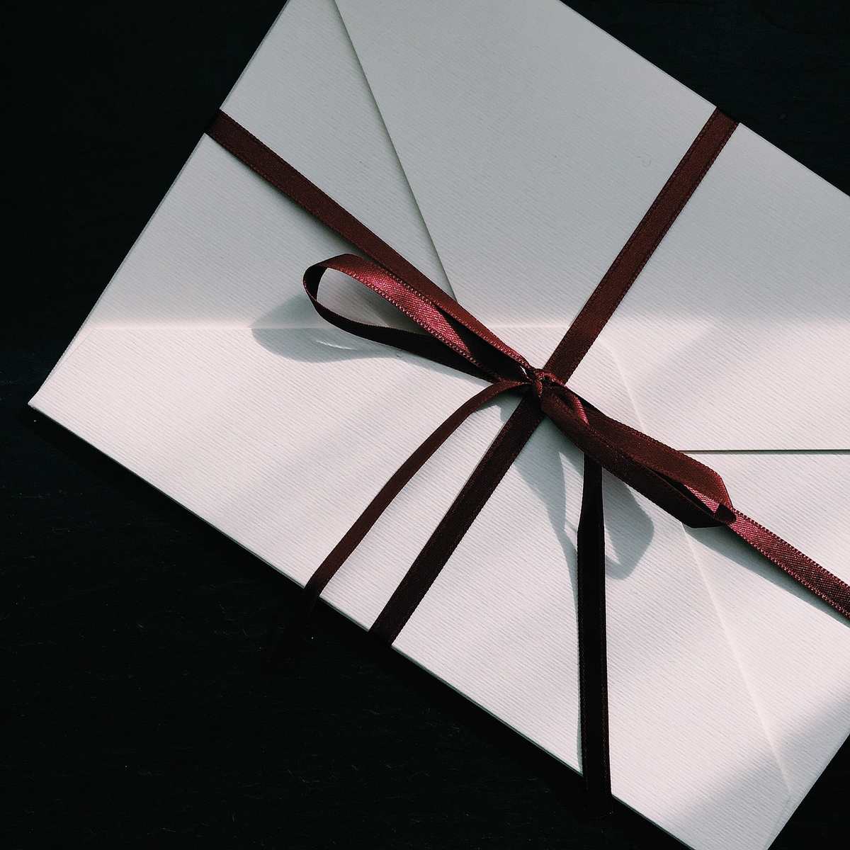 Enveloppe blanche nouée avec un ruban marron sur fond noir