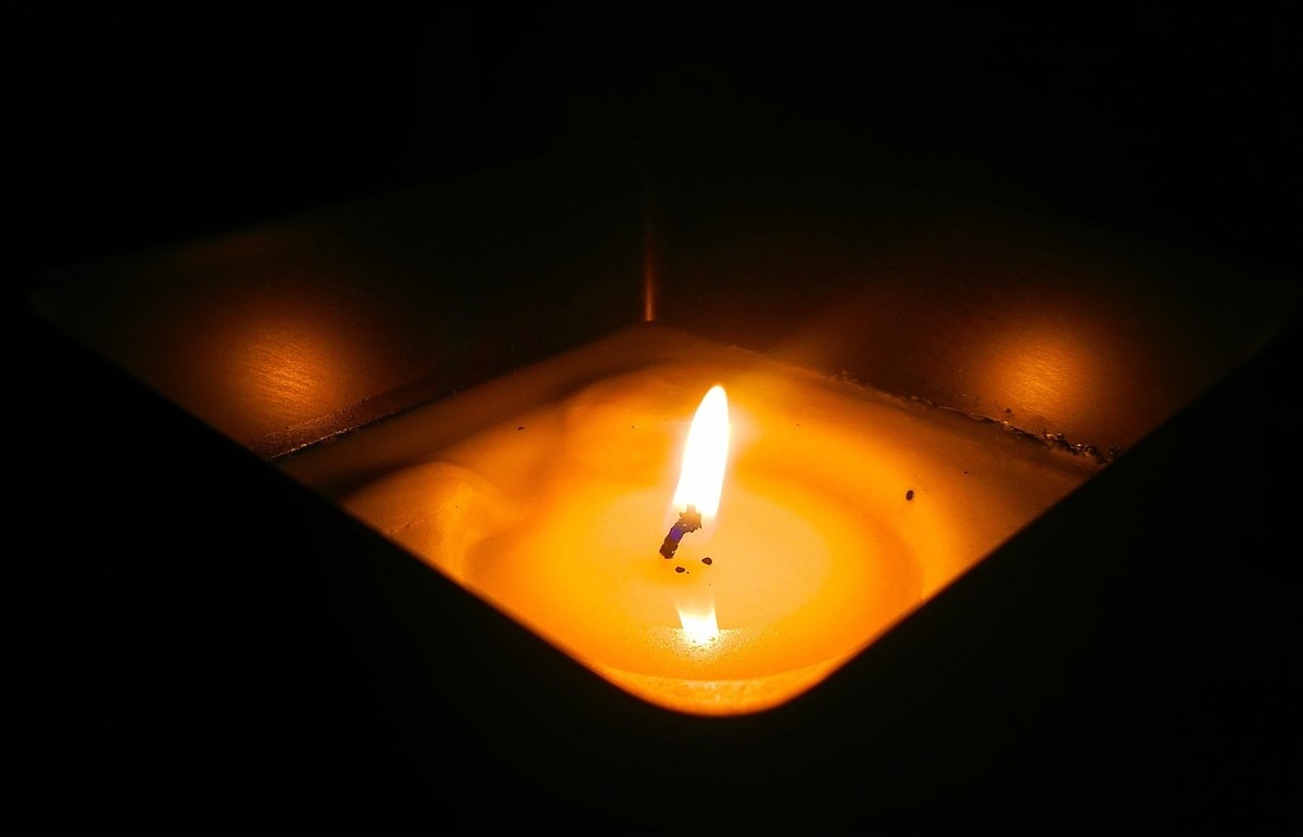 Bougie allumée dans un support carré, lumière chaude dans l'obscurité Bougie allumée dans un support carré, lumière chaude dans l'obscurité