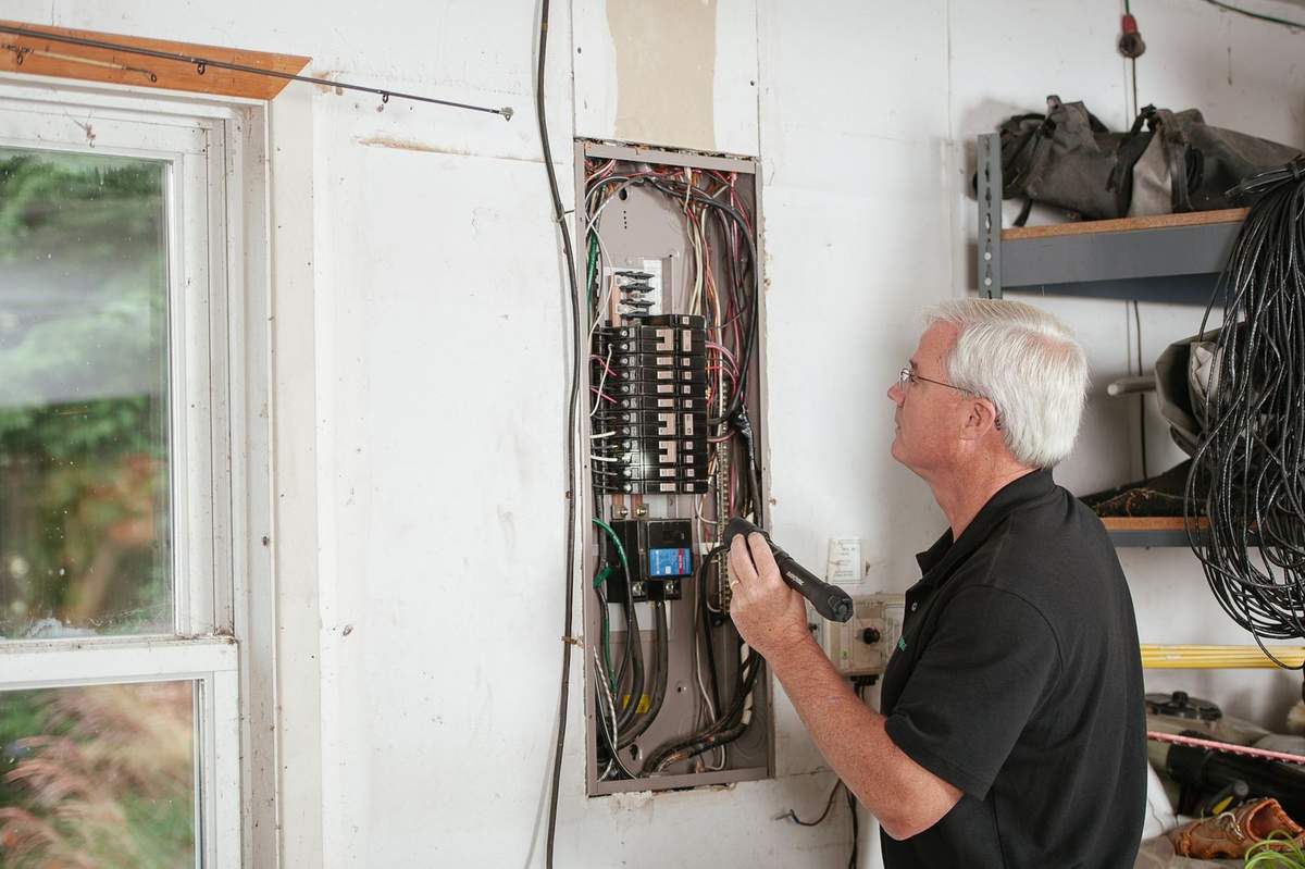 Un homme examine un tableau électrique avec des outils dans une pièce blanche