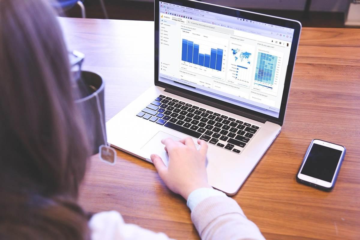 Femme utilisant un laptop avec graphiques et un smartphone sur une table en bois