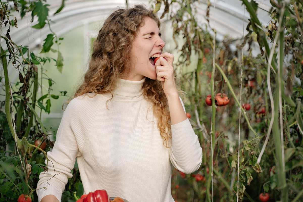 Femme savourant une tomate dans une serre entourée de plantes