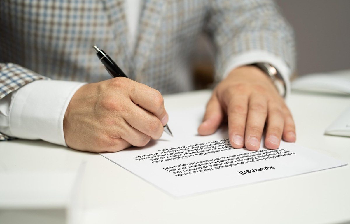 Homme écrivant sur un document avec un stylo noir à la table Homme écrivant sur un document avec un stylo noir à la table