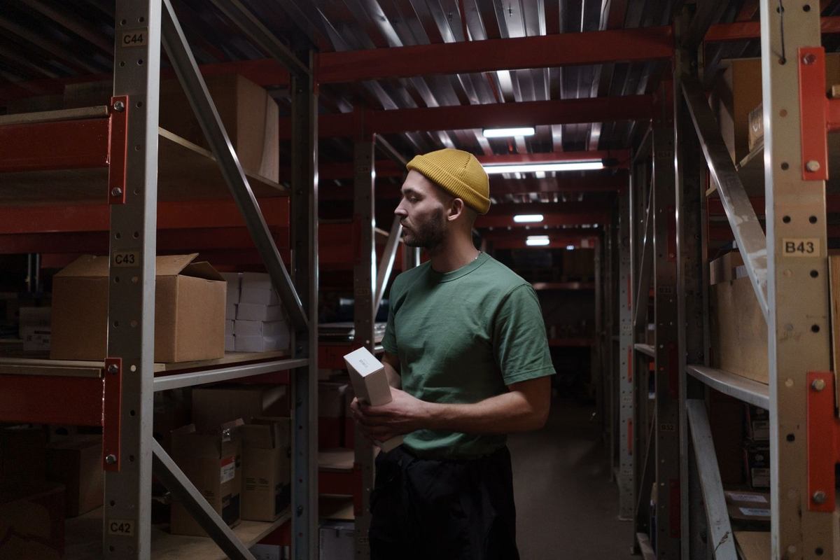 Homme inspecte des boîtes dans un entrepôt avec des étagères métalliques Homme inspecte des boîtes dans un entrepôt avec des étagères métalliques