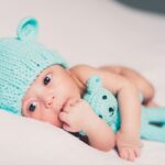 Un nourrisson avec bonnet d'ours et peluche bleue sur drap blanc