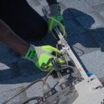 Technicien en gants jaunes ajuste un équipement avec câbles sur un revêtement gris