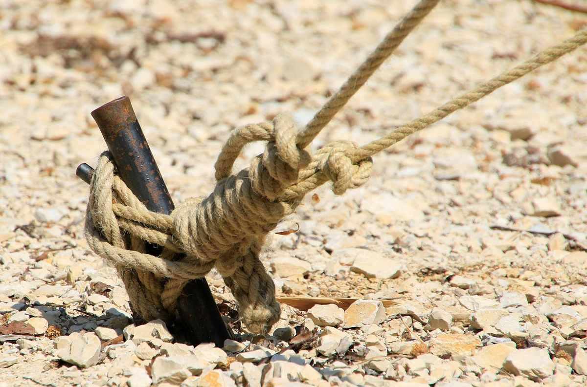 Corde nouée autour d'un morceau de bois sur un terrain rocheux Corde nouée autour d'un morceau de bois sur un terrain rocheux
