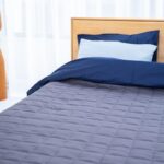 Un lit fait avec draps bleus, coussins, et lampe design