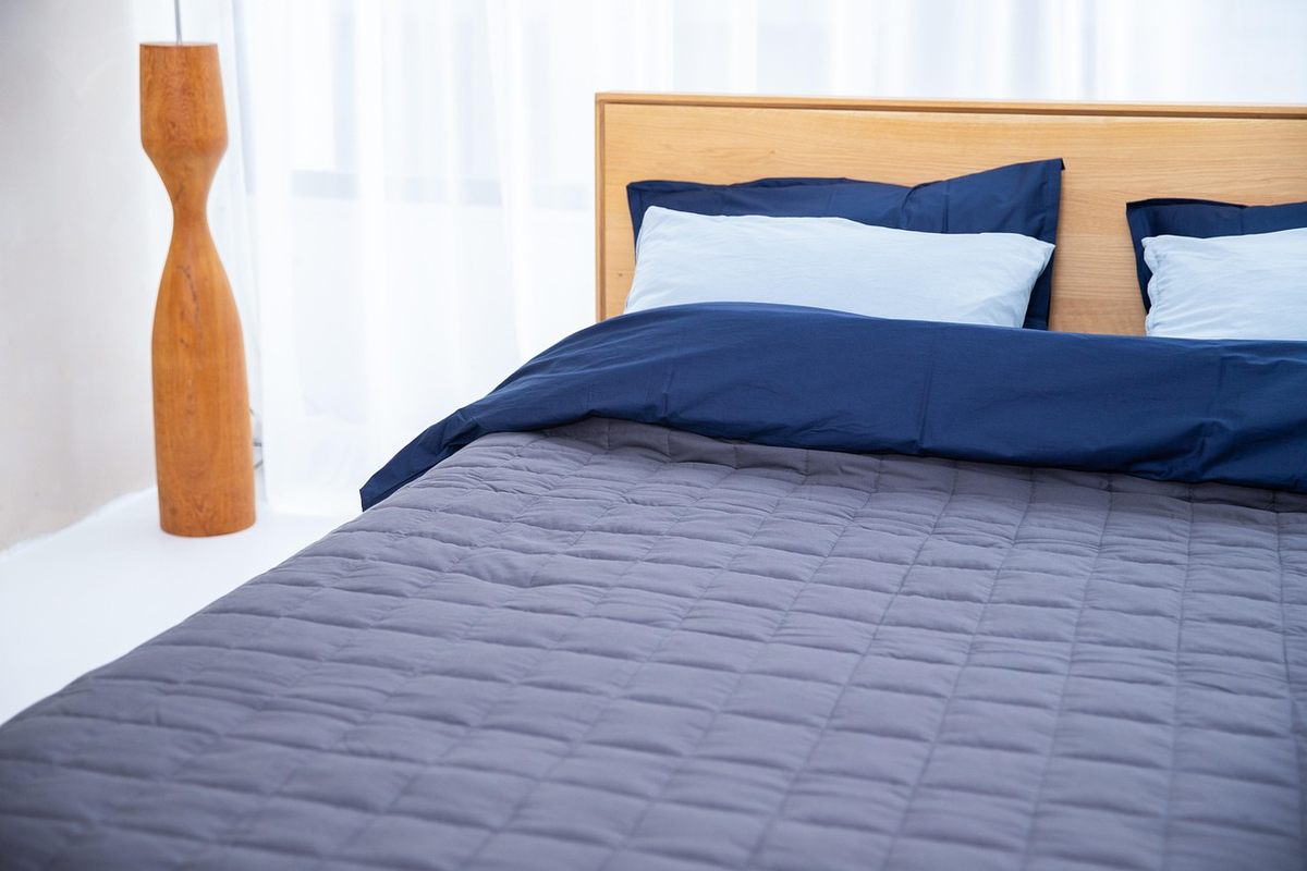 Un lit fait avec draps bleus, coussins, et lampe design