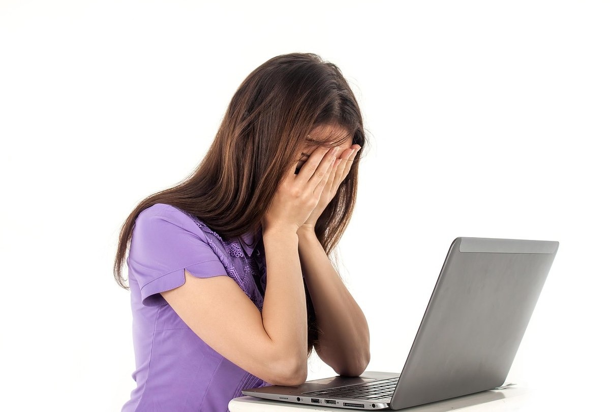 femme stressée devant ordinateur, mains sur visage, expression de désespoir femme stressée devant ordinateur, mains sur visage, expression de désespoir