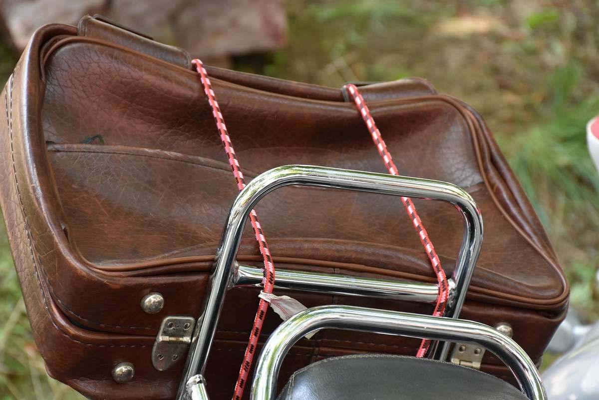 Valises en cuir marron attachées avec des cordes rouges sur un porte-bagages chromé de motocyclette Valises en cuir marron attachées avec des cordes rouges sur un porte-bagages chromé de motocyclette