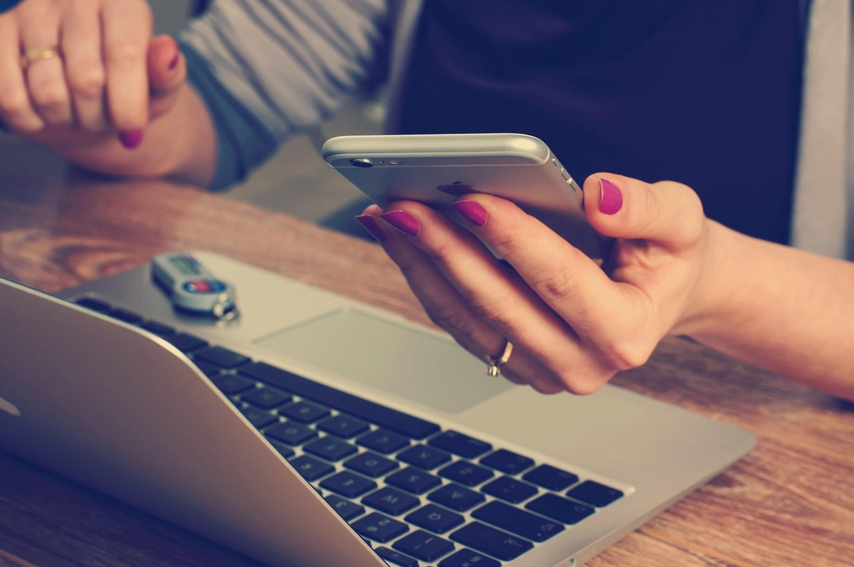 Une main tenant un smartphone au-dessus d'un ordinateur portable Une main tenant un smartphone au-dessus d'un ordinateur portable