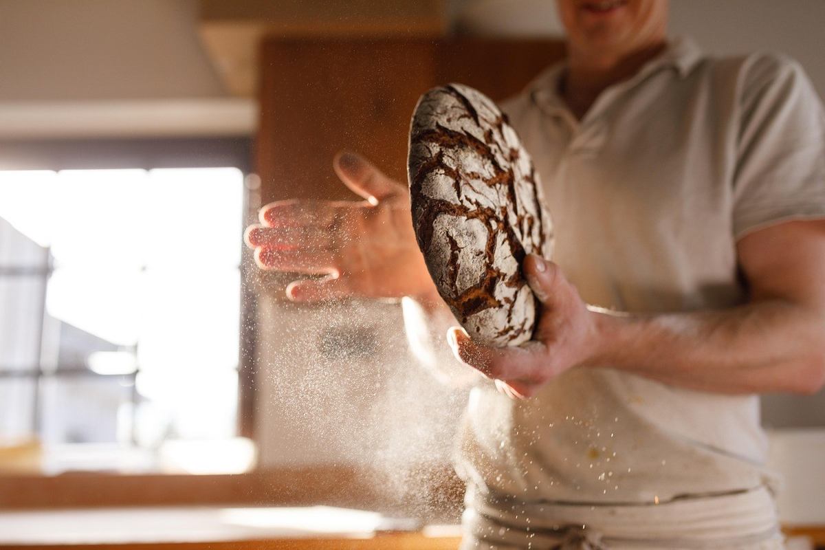 Homme fariné tient un pain rustique dans une cuisine lumineuse Homme fariné tient un pain rustique dans une cuisine lumineuse