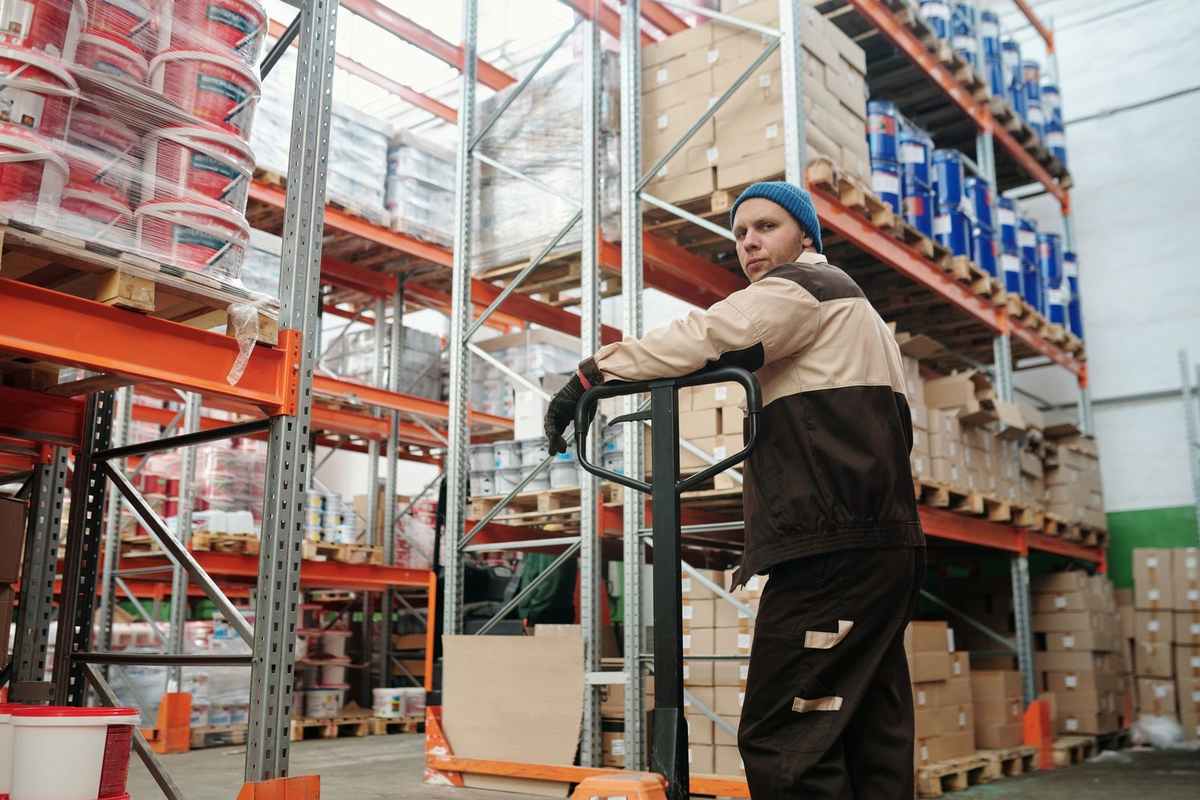 Employé sur chariot élévateur dans un entrepôt rempli de palettes et de produits Employé sur chariot élévateur dans un entrepôt rempli de palettes et de produits
